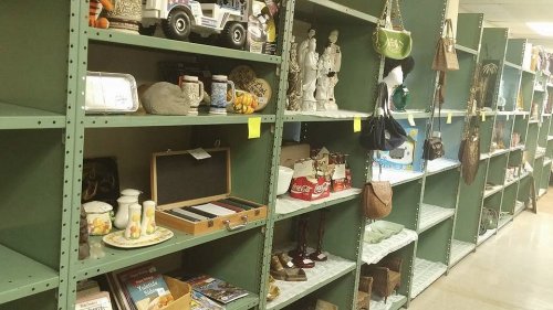 A row of green shelves filled with various items, including decor, bags, and collectibles in a thrift store.