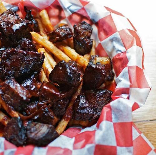 A basket lined with red and white checkered paper filled with crispy fries and pieces of dark, glazed meat.