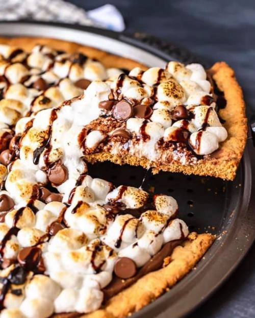 A delicious s'mores dessert pizza topped with toasted marshmallows, chocolate chips, and drizzled with chocolate sauce.