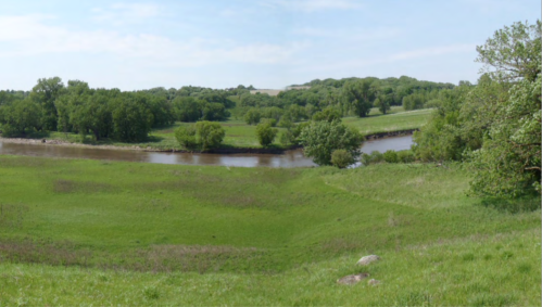 A serene landscape featuring a winding river surrounded by lush green fields and trees under a clear blue sky.