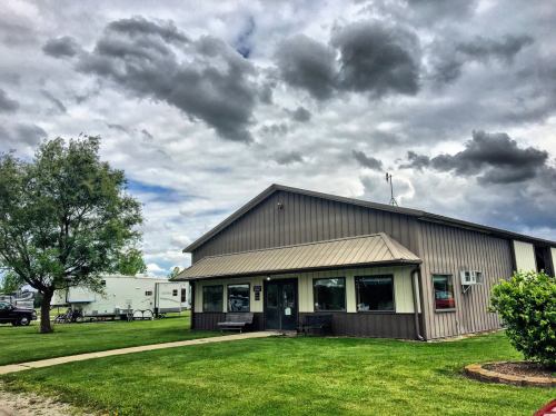 A modern building with a metal exterior, surrounded by green grass and cloudy skies. A trailer is visible in the background.