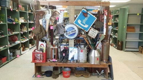 A display of vintage items, including signs, tools, and collectibles, arranged on a wooden table in a shop.