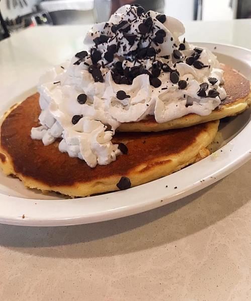 A plate of two fluffy pancakes topped with whipped cream and chocolate chips.