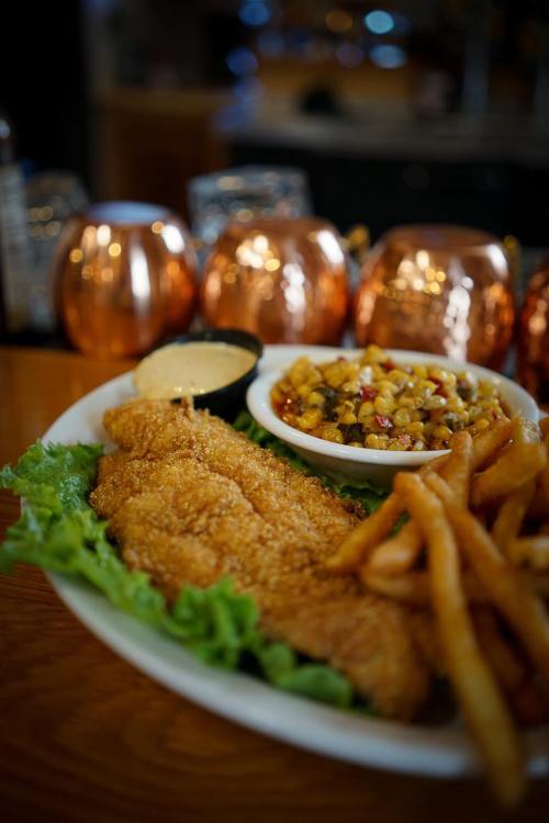 A plate of crispy fried fish fillets with fries and a side of corn salad, served on a bed of lettuce.