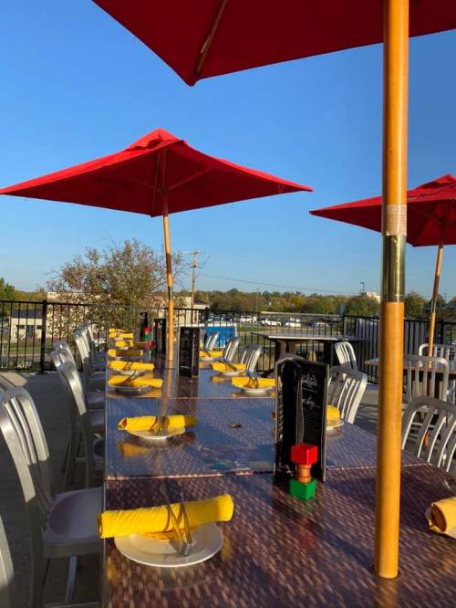 A sunny outdoor dining area with a long table set with yellow napkins and red umbrellas.