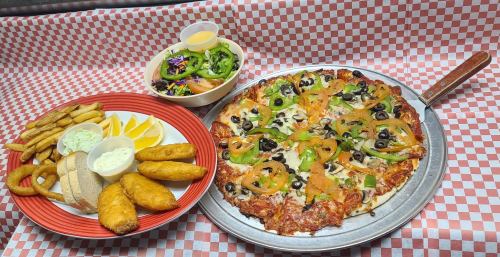 A pizza topped with olives, green peppers, and onions, served with a side of fries, salad, and dipping sauces.