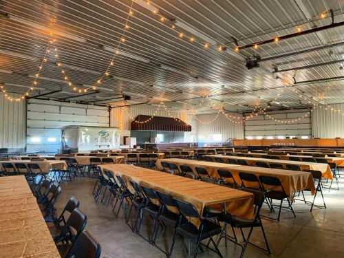 A spacious event hall with long tables, chairs, and string lights hanging from the ceiling.