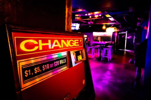 A brightly lit change machine in a dimly lit bar, with colorful lights and empty stools in the background.