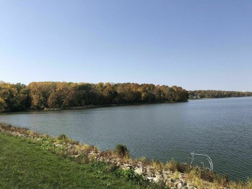 A serene lake surrounded by trees with autumn foliage under a clear blue sky.