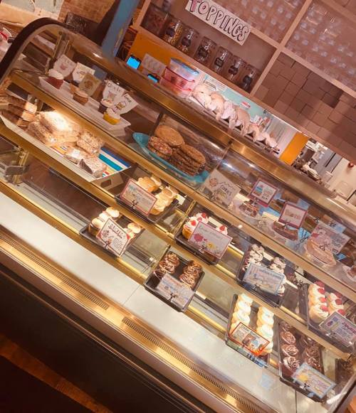 A display case filled with various baked goods, including cookies, cupcakes, and desserts, with colorful labels.