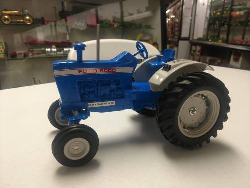 A blue and white model of a Ford 8000 tractor displayed on a table, showcasing detailed features and wheels.