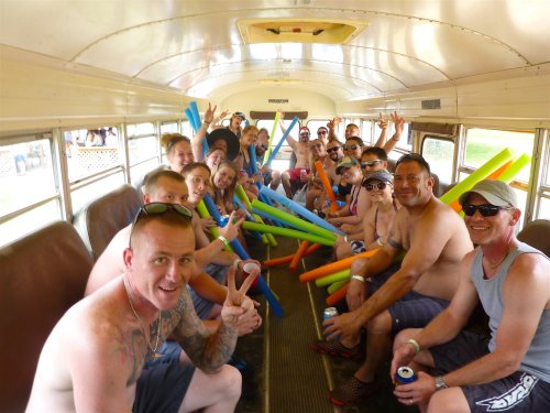 A group of people on a bus, smiling and holding colorful pool noodles, enjoying a fun gathering.