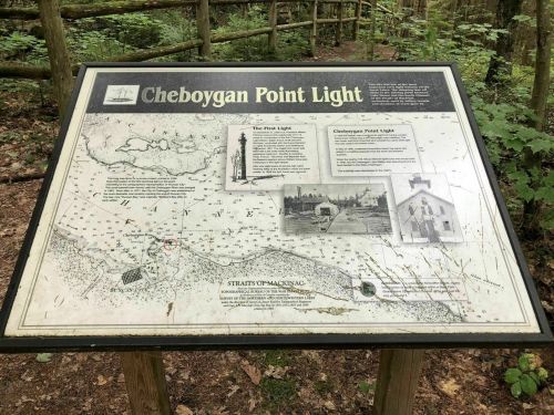 Sign detailing Cheboygan Point Light, featuring a map and historical information, surrounded by trees in a wooded area.