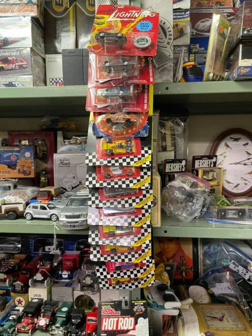 A collection of toy cars displayed in packaging, stacked vertically on a shelf among various collectibles.