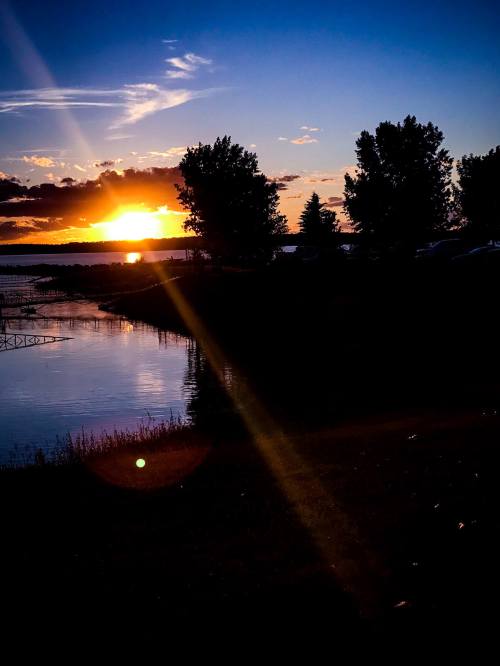 Sunset over a calm lake, with silhouettes of trees and a vibrant sky reflecting on the water.