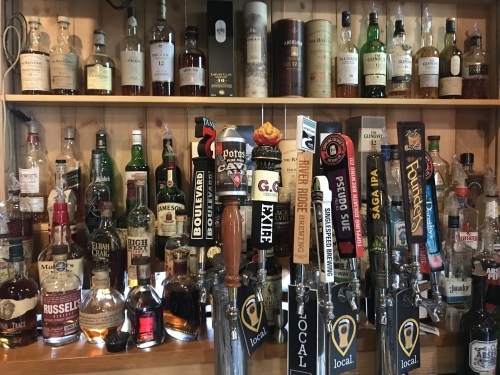 A wooden bar shelf filled with various bottles of liquor and beer taps, showcasing a wide selection of drinks.