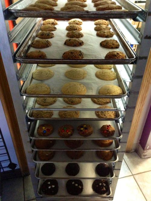 A metal rack filled with various types of freshly baked cookies on parchment paper.