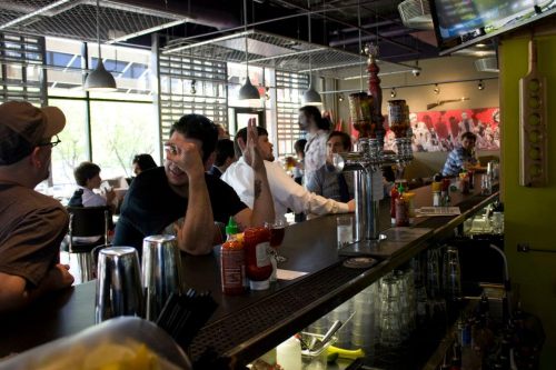 A lively bar scene with patrons chatting at the counter, drinks and condiments visible, and a vibrant atmosphere.