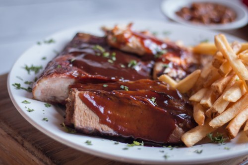 A plate of barbecue ribs with sauce, served alongside crispy fries and a small bowl of beans.