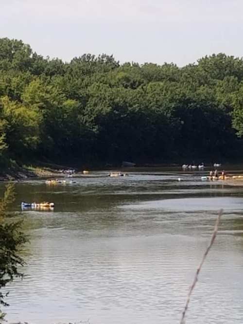 A serene river scene with boats on the water, surrounded by lush green trees and a clear sky.