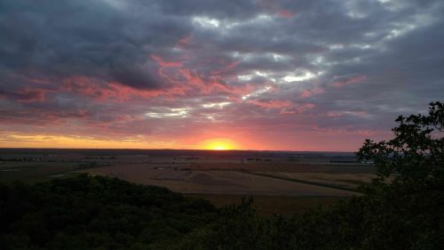A vibrant sunset over a vast landscape, with colorful clouds and fields stretching into the distance.