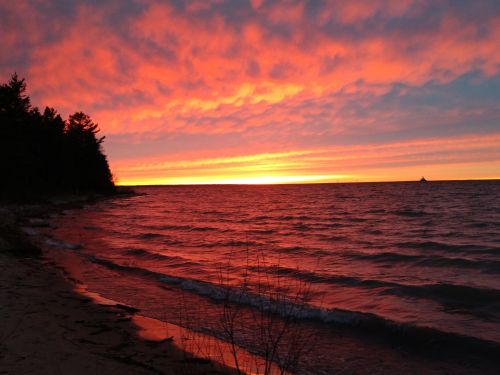 A vibrant sunset over a calm lake, with colorful clouds reflecting on the water and a shoreline lined with trees.