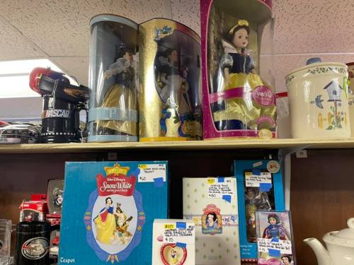 Dolls and collectibles featuring Snow White displayed on a shelf in a store, with price tags visible.