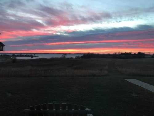 A vibrant sunset over a calm waterway, with colorful clouds and a grassy foreground.