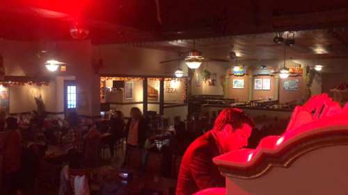 A dimly lit restaurant scene with a man at a counter, people dining, and festive decorations in the background.