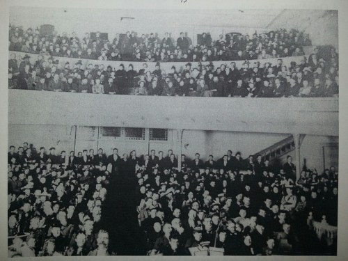 A large crowd of people seated in a theater, with multiple levels of seating visible.