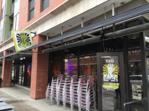 Exterior of Zombie Burger restaurant with stacked chairs outside and a colorful sign above the entrance.