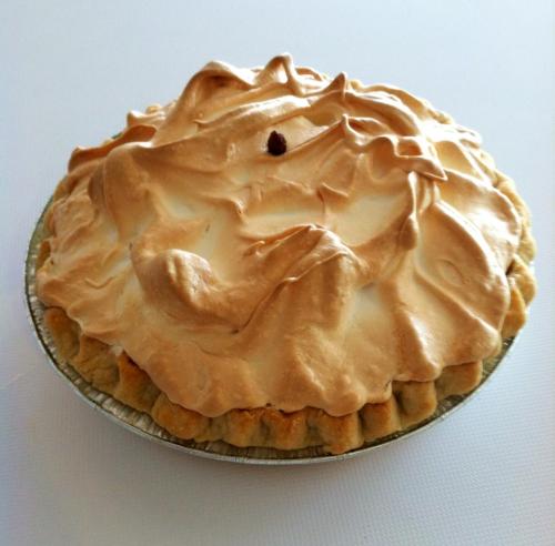 A golden-brown meringue pie with a fluffy topping, resting in a silver pie dish on a white surface.