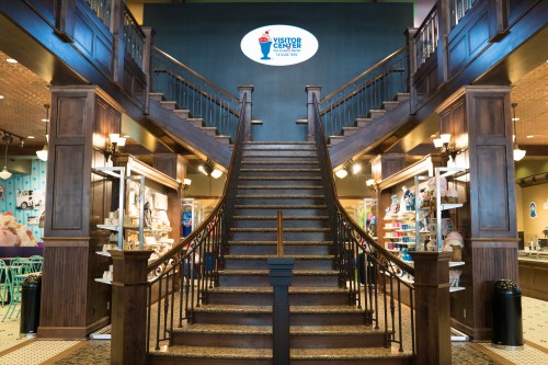 Interior of a visitor center featuring a grand staircase and displays on either side, with a logo on the wall above.