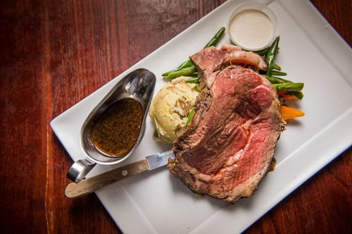 A plate featuring a large slice of roast beef, mashed potatoes, green beans, and a side of gravy.