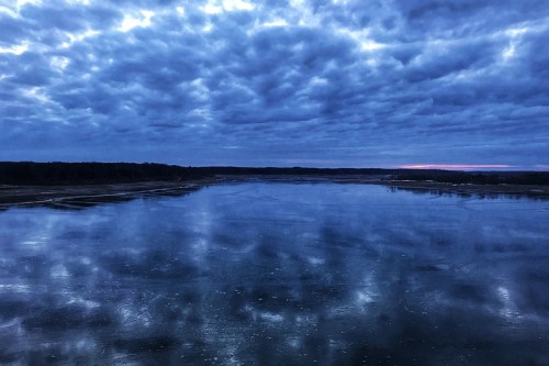 A tranquil river scene at dusk, reflecting a cloudy sky with hints of twilight colors on the water's surface.