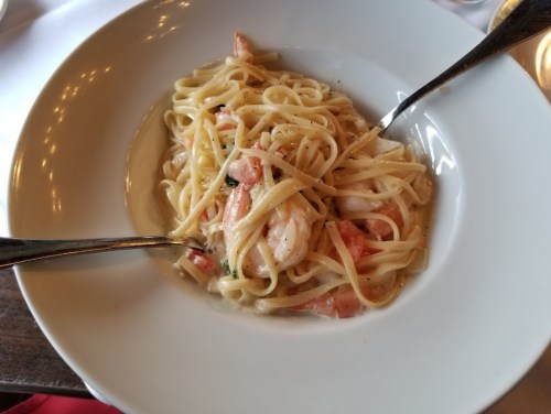 A bowl of linguine pasta with shrimp and tomatoes, garnished with herbs, served with two silver forks.