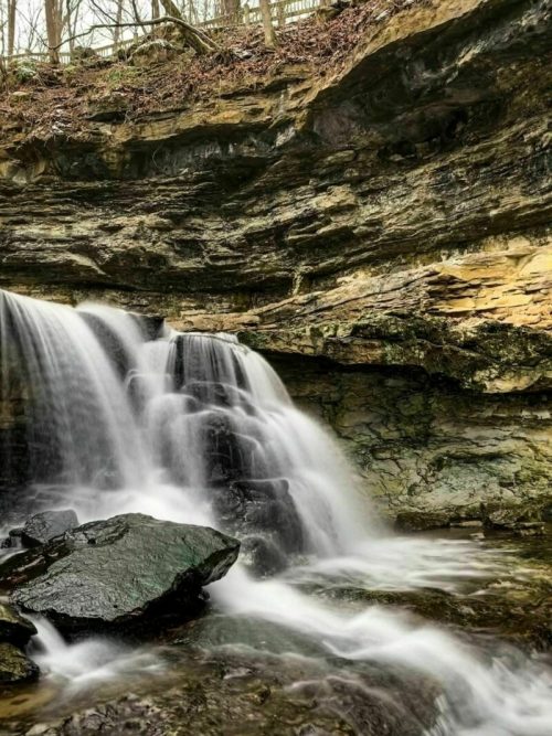 A serene waterfall cascades over rocky cliffs, surrounded by lush greenery and textured stone formations.