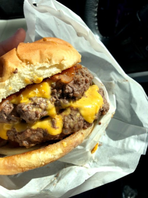 A close-up of a juicy cheeseburger with melted cheese, stacked beef patties, and a soft bun, held in a hand.
