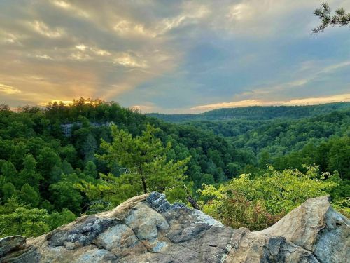 A scenic view of a lush green valley at sunset, with rocky outcrops and a cloudy sky in the background.