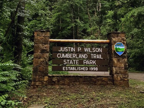 Sign for Justin P. Wilson Cumberland Trail State Park, surrounded by lush greenery, established in 1998.
