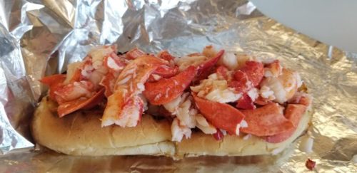 A lobster roll filled with chunks of lobster meat on a toasted bun, wrapped in foil.