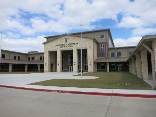 Exterior view of Churchill Fulshear Jr. High School, featuring a stone facade and grassy area under a cloudy sky.