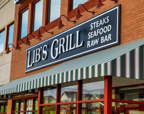 Sign for Lib's Grill featuring steaks, seafood, and a raw bar, with a striped awning and brick facade.