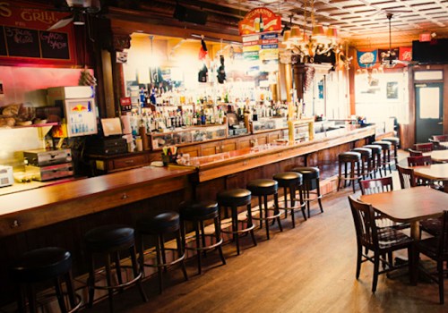 A cozy bar interior with a long wooden counter, stools, and shelves stocked with various drinks.