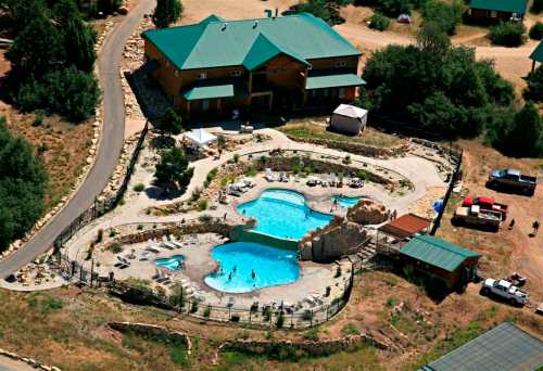 Aerial view of a large pool area with rock formations, surrounded by greenery and a lodge in the background.