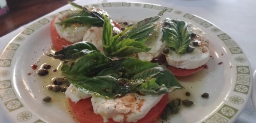 A plate of fresh mozzarella, tomatoes, and basil drizzled with olive oil and sprinkled with capers and spices.