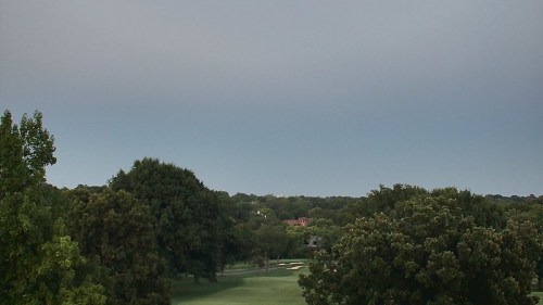 A view of a golf course surrounded by trees under a cloudy sky.