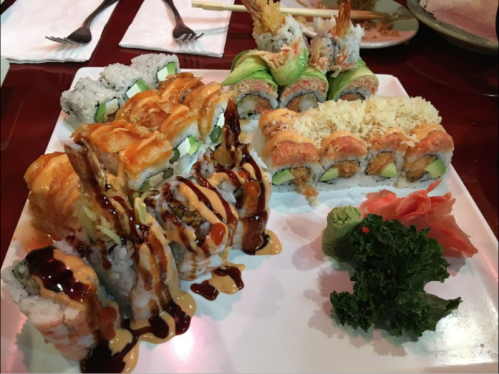 A plate of assorted sushi rolls, including shrimp, avocado, and tempura, garnished with wasabi and pickled ginger.