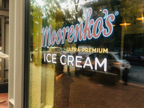 Sign for Maorenko's Ultra-Premium Ice Cream, displayed on a storefront window with a city street reflection.