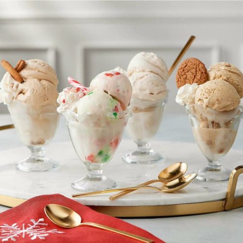 Four ice cream sundaes in glass dishes, featuring various flavors and toppings, on a marble surface with gold accents.